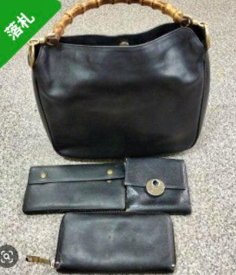 A black Gucci bamboo-handle handbag and three black wallets displayed on a carpeted surface.