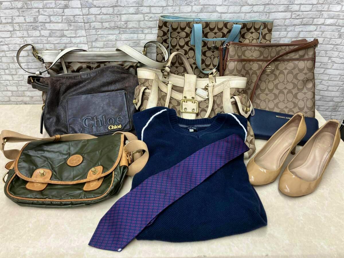 Assorted brand bags, a sweater, a tie and a pair of beige heels arranged on a table as a bulk set.