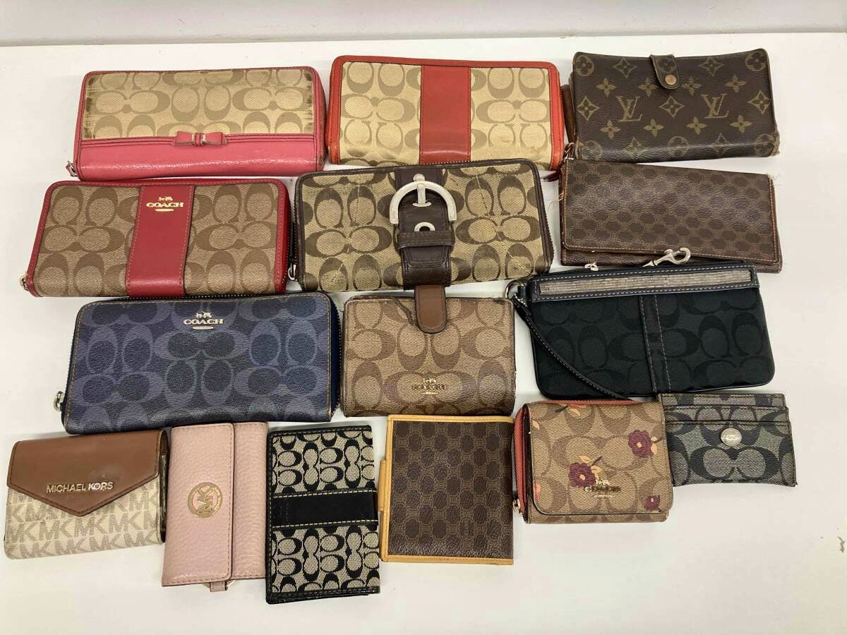 Flat lay of multiple assorted wallets, card cases, and small pouches including Coach and other designer brands on a white background.