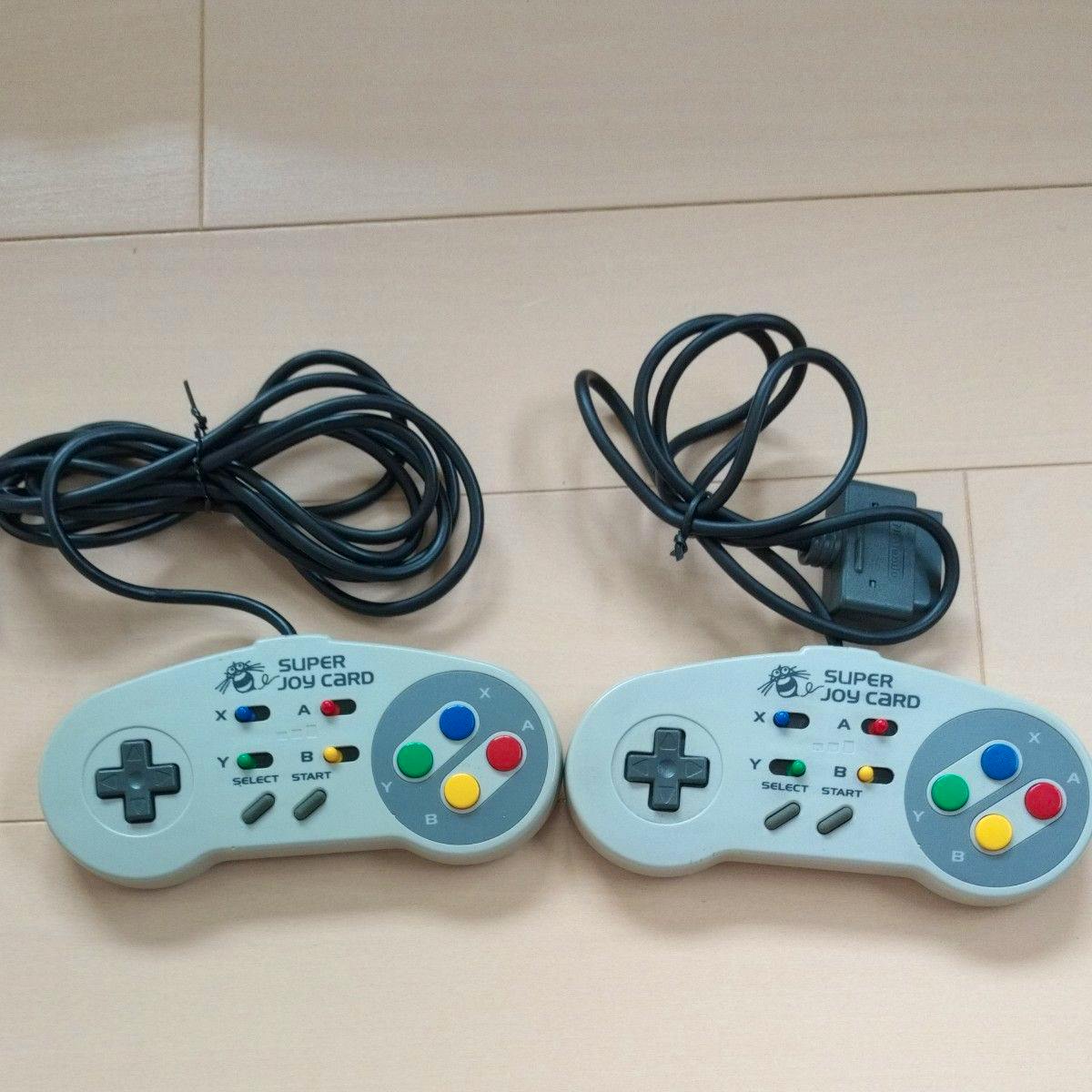 Two SFC "SUPER JOY CARD" wired controllers shown side by side with their buttons, D-pads, and cables visible.