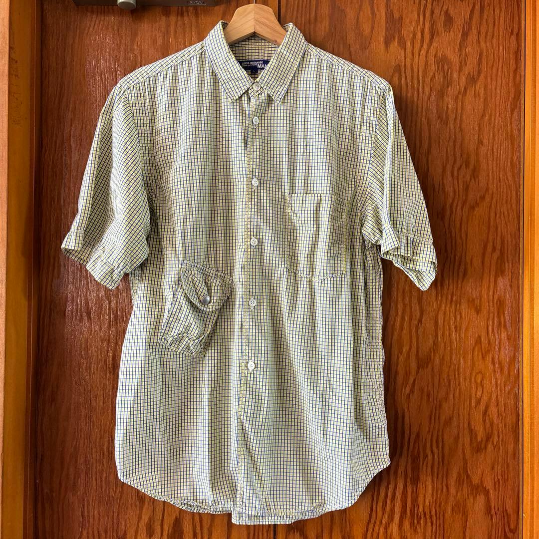 Front view of a men's short-sleeve cotton checkered button-up shirt with a lower cargo pocket hanging on a wooden hanger.