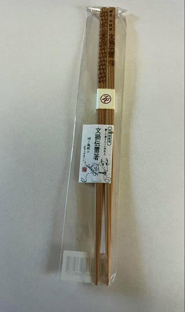 Unopened pair of wooden chopsticks in clear plastic packaging with a visible '文禍伝雷' label.