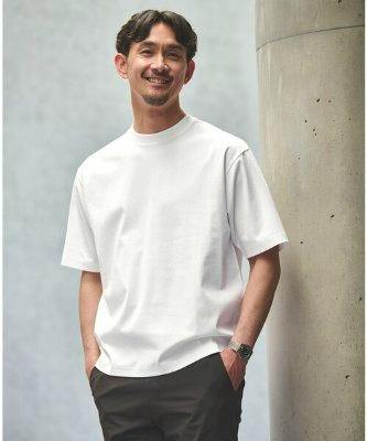 Male model wearing a white short-sleeve T-shirt standing with hands in his pockets beside a concrete pillar.