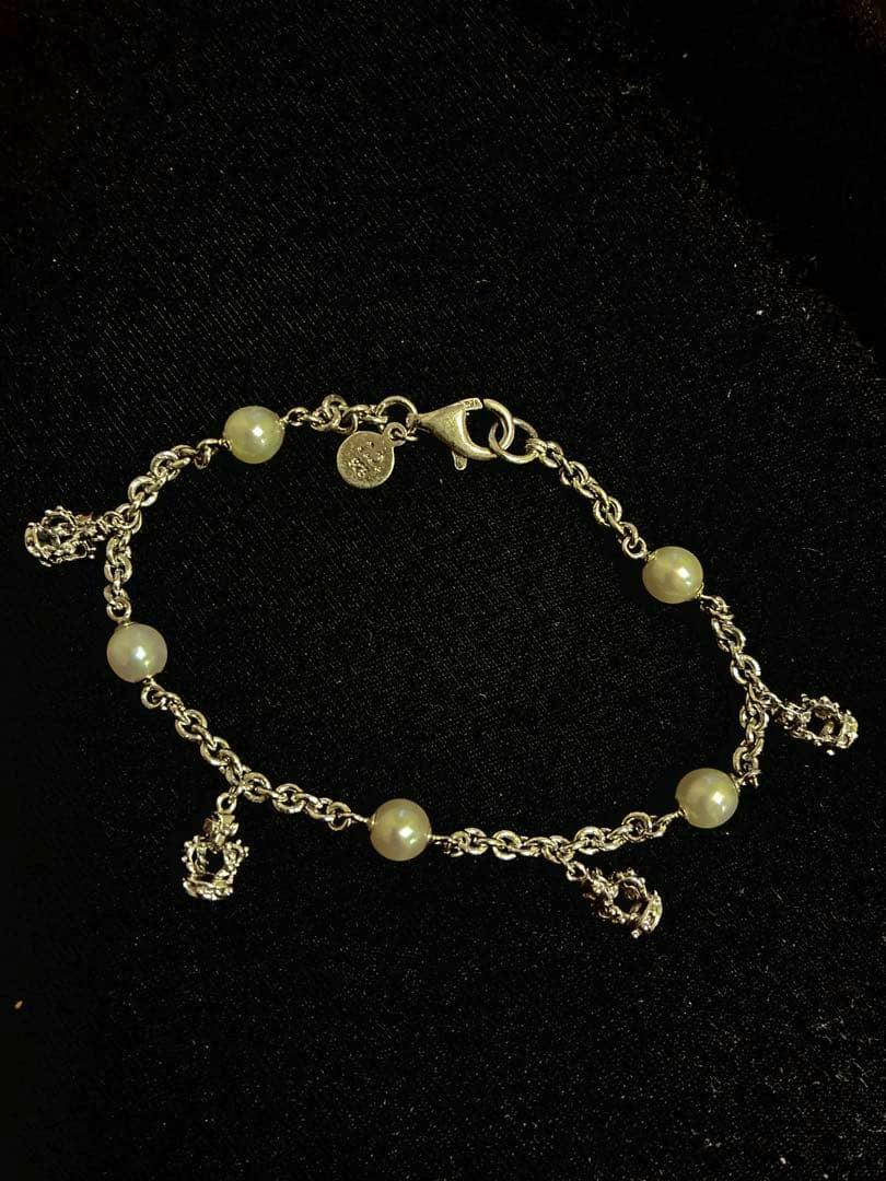 Justin Davis bracelet with a metal chain, pearl-like beads, and small crown charms on black fabric.