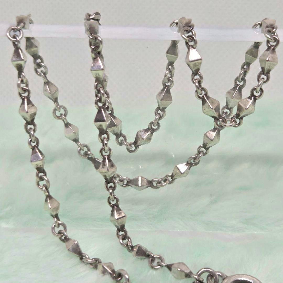 Close-up photo of the silver-tone CURIO chain bracelet showing its geometric links and clasp draped over a clear display rod on a pale background.