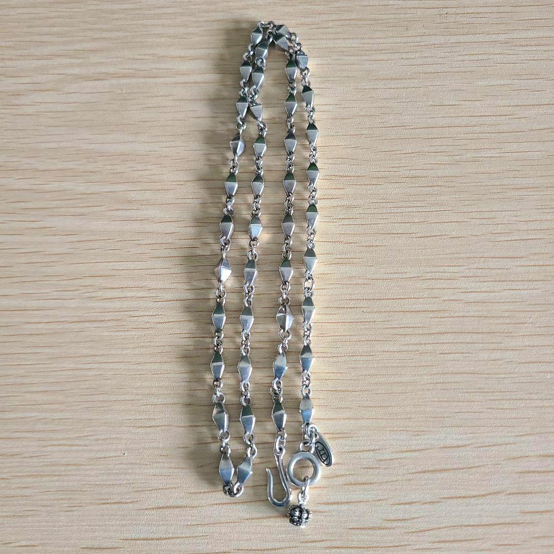 Metal Justin Davis Piccadilly chain laid flat showing the full chain and its clasp on a wooden surface.