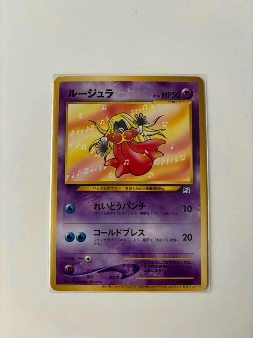 Front of the ルージュラ promo Pokémon trading card from "ポケモンカードになったワケ 3巻" photographed on a white background.