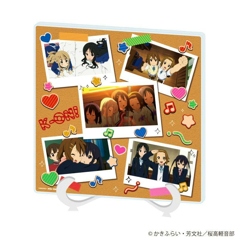 A square acrylic art board showing a corkboard-style collage of TV anime 'K-On!' scene illustrations with colorful stickers and a clear plastic stand.