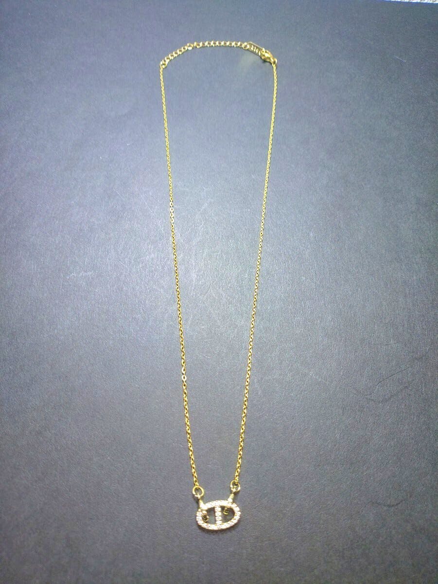 Gold-colored chain necklace with a small oval pendant encrusted with stones laid flat on a dark background.
