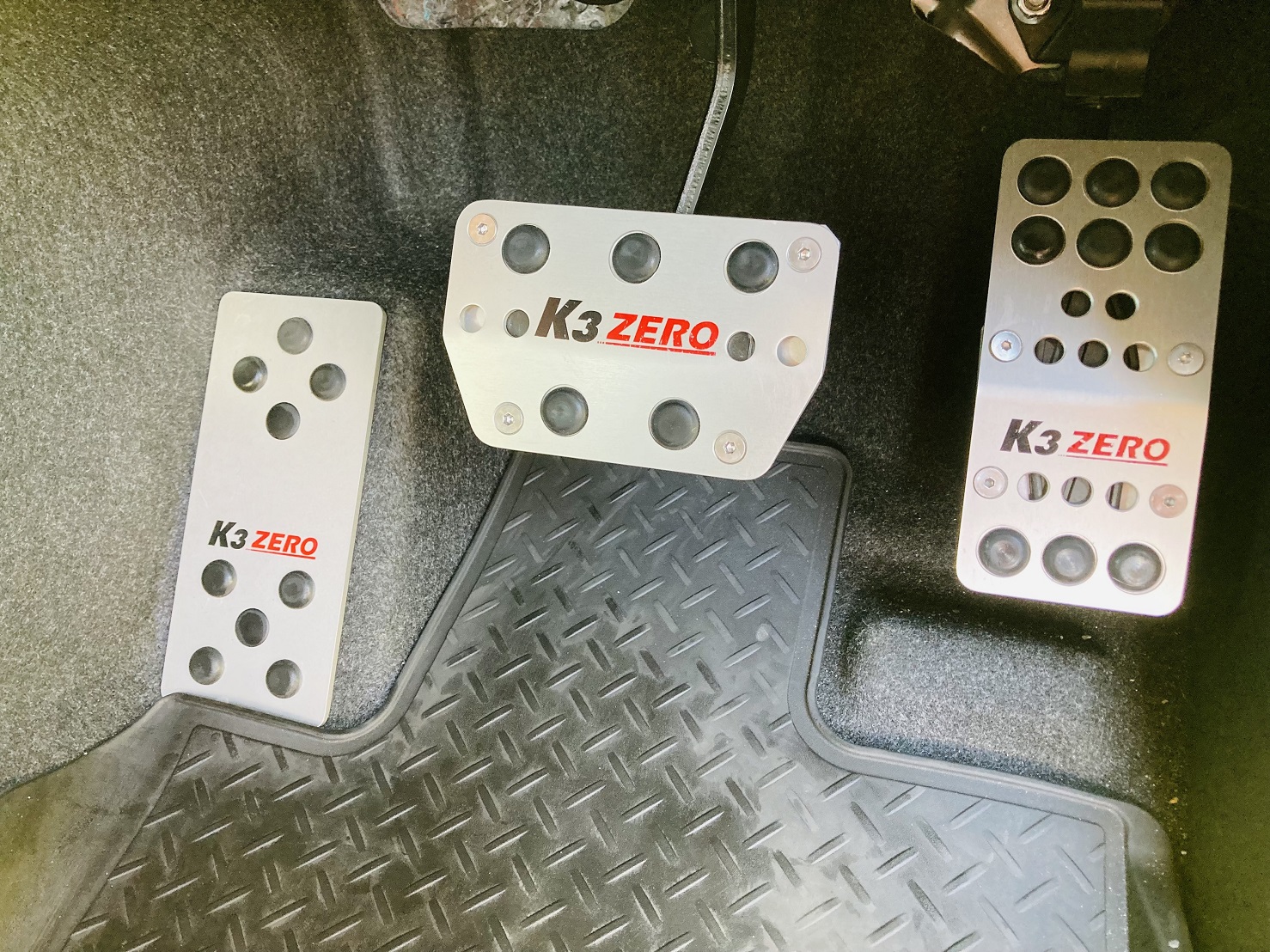 K3 ZERO automatic pedals installed in a car driver's footwell, showing three metal pedal covers (footrest, brake, accelerator).