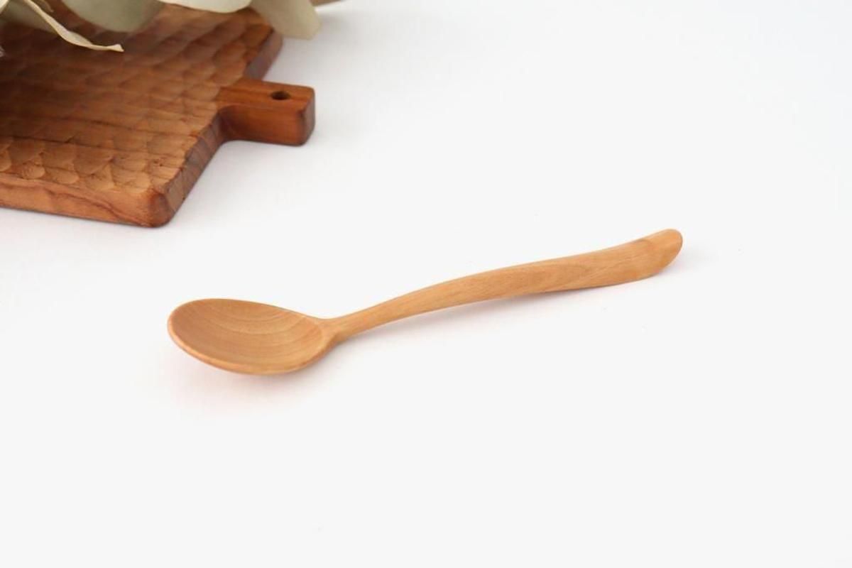 Wooden soup spoon shown on a white background with part of a wooden board visible.
