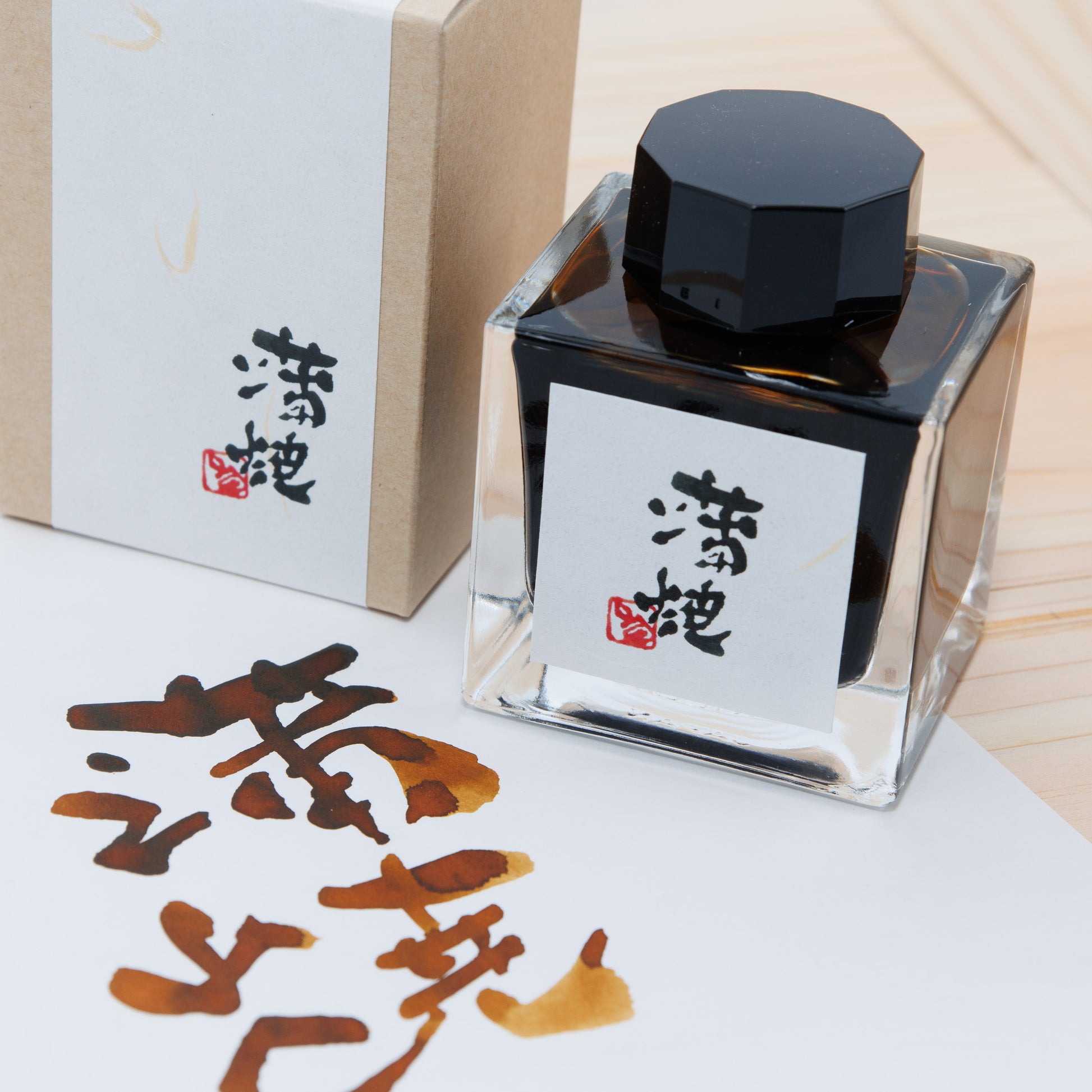 A glass bottle of Kabayaki fountain pen ink shown with its box and a brown calligraphy swatch on paper.