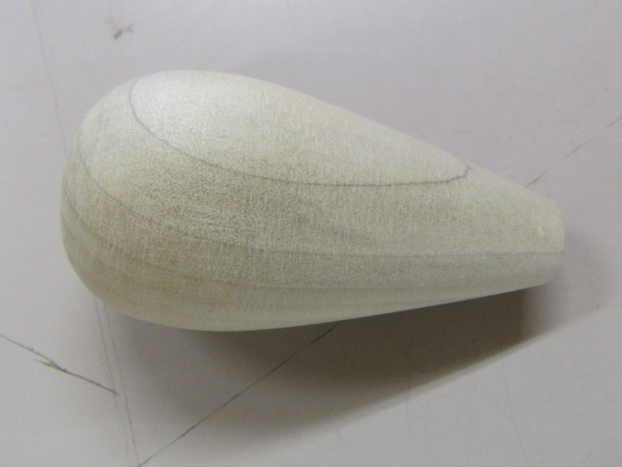Side view of a light wooden archery blunt tip (かぶら) showing its teardrop shape and surface pencil guide lines.