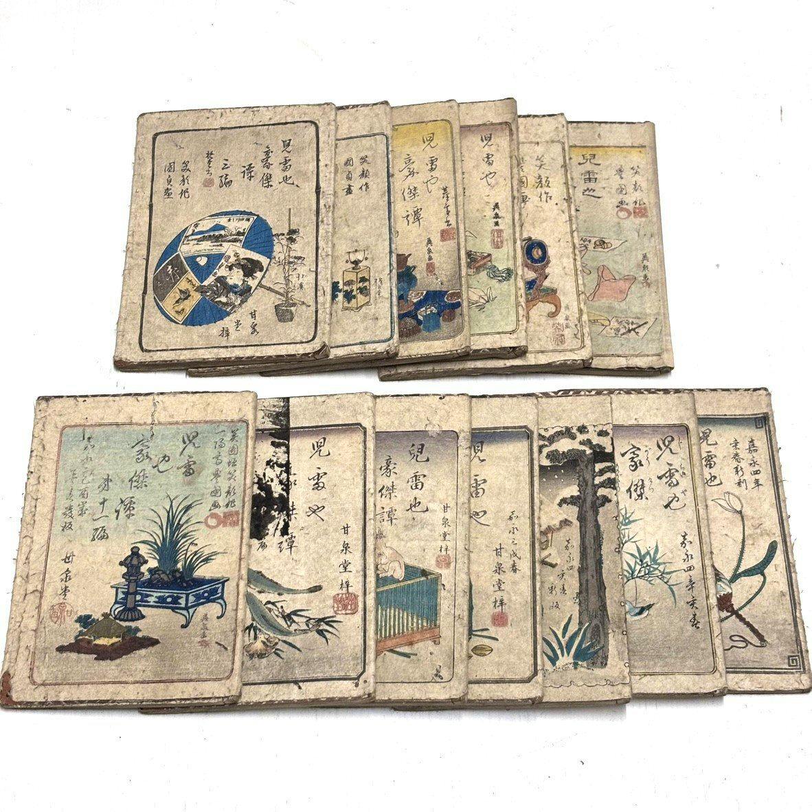 Stacked antique Japanese book set (13 volumes) showing illustrated front covers and age-related wear.