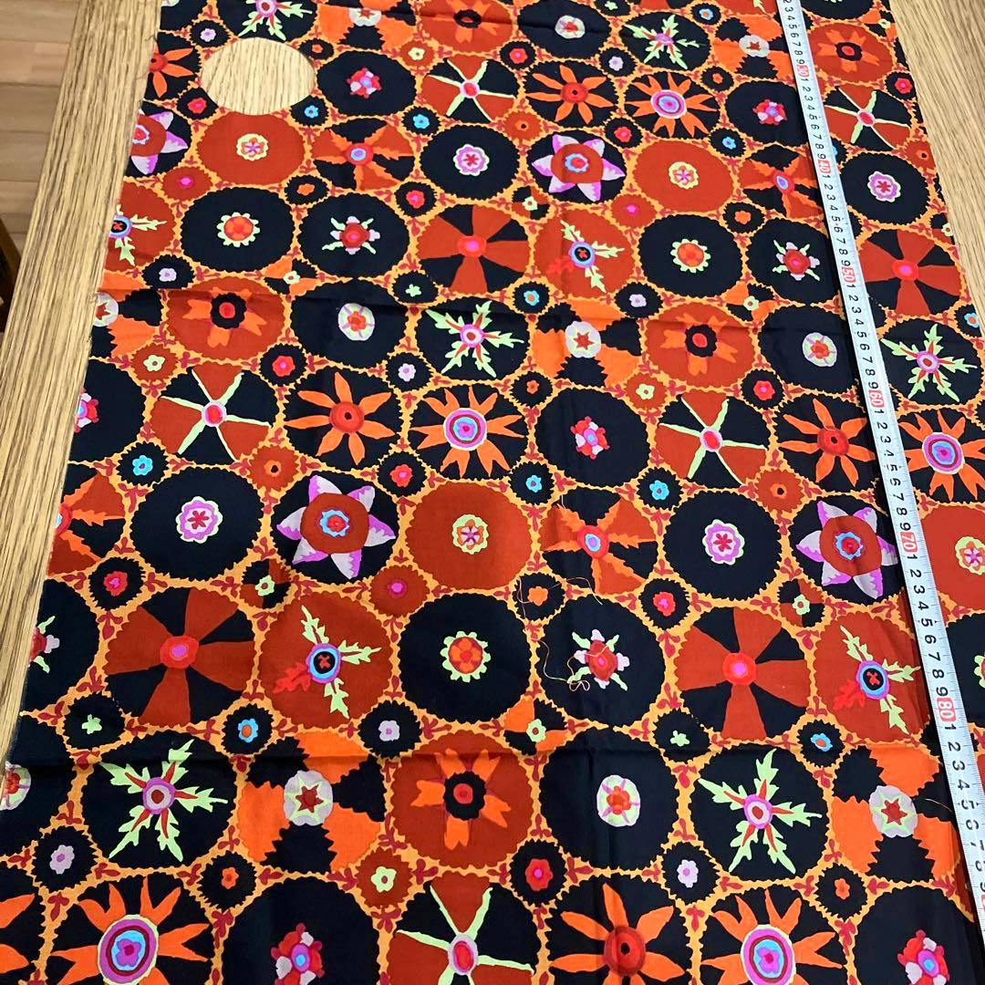 A rectangular piece of Kaffe Fassett geometric patterned cotton fabric with orange and black circular motifs laid flat on a table with a measuring tape along one side.
