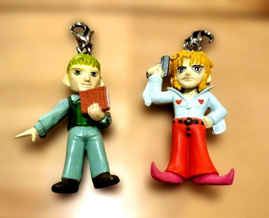 Two small plastic figure keychain charms shown side by side on a beige background.