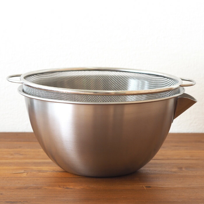 A stainless steel mixing bowl with a matching mesh strainer sitting together on a wooden surface.