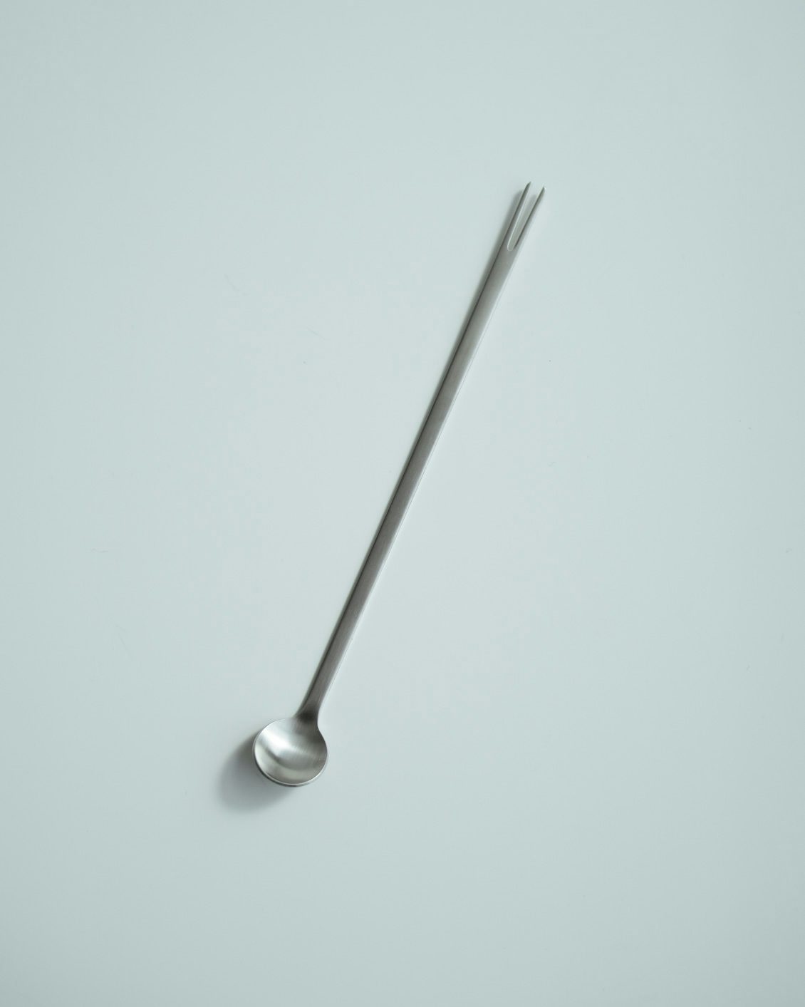 A long metal tasting spoon with a small round bowl shown on a plain light background.