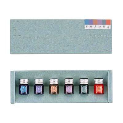 A rectangular box containing six mini fountain-pen ink bottles arranged side by side with a month color strip labeled 7–12.