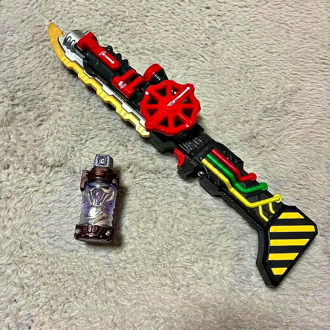 An imitation sword (Kamen Rider Build Steam Blade) toy lying on a carpeted surface with a small clear bottle accessory beside it.