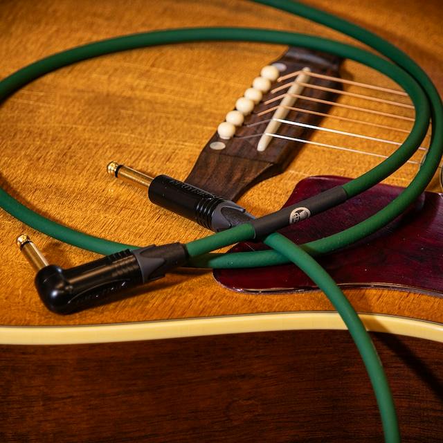 A green 3m acoustic/AUX cable with straight and right-angle 1/4-inch plugs coiled on an acoustic guitar.