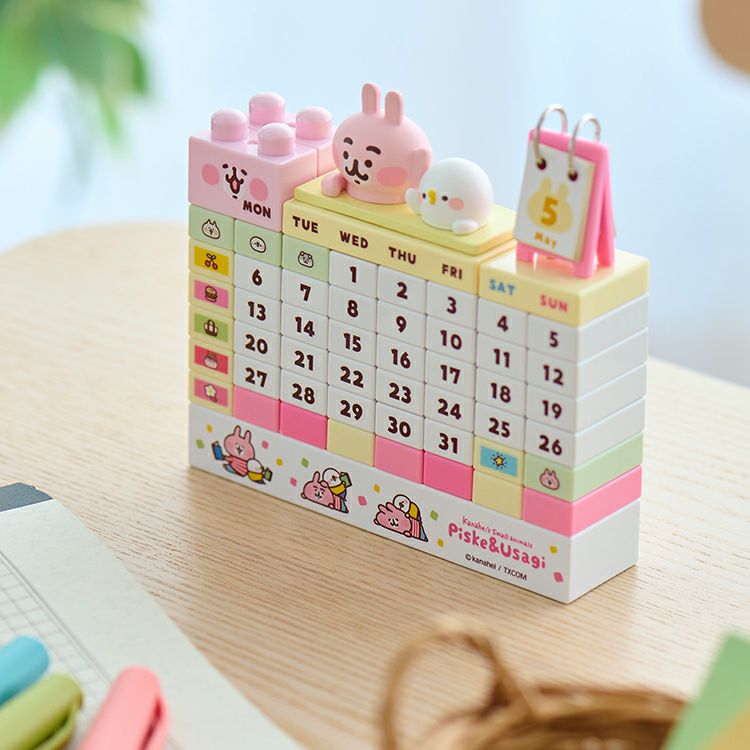 Photo of the block calendar featuring Pisuke and Usagi character figures atop numbered weekday blocks on a wooden table.