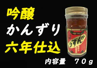A glass jar of the chilli sauce (70 g) with a red label shown on a black background alongside Japanese text.