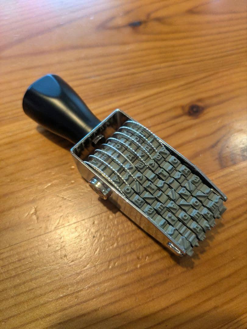 Rotating kaoiro 顔文字 stamp with multiple rubber character wheels and a black handle resting on a wooden surface.