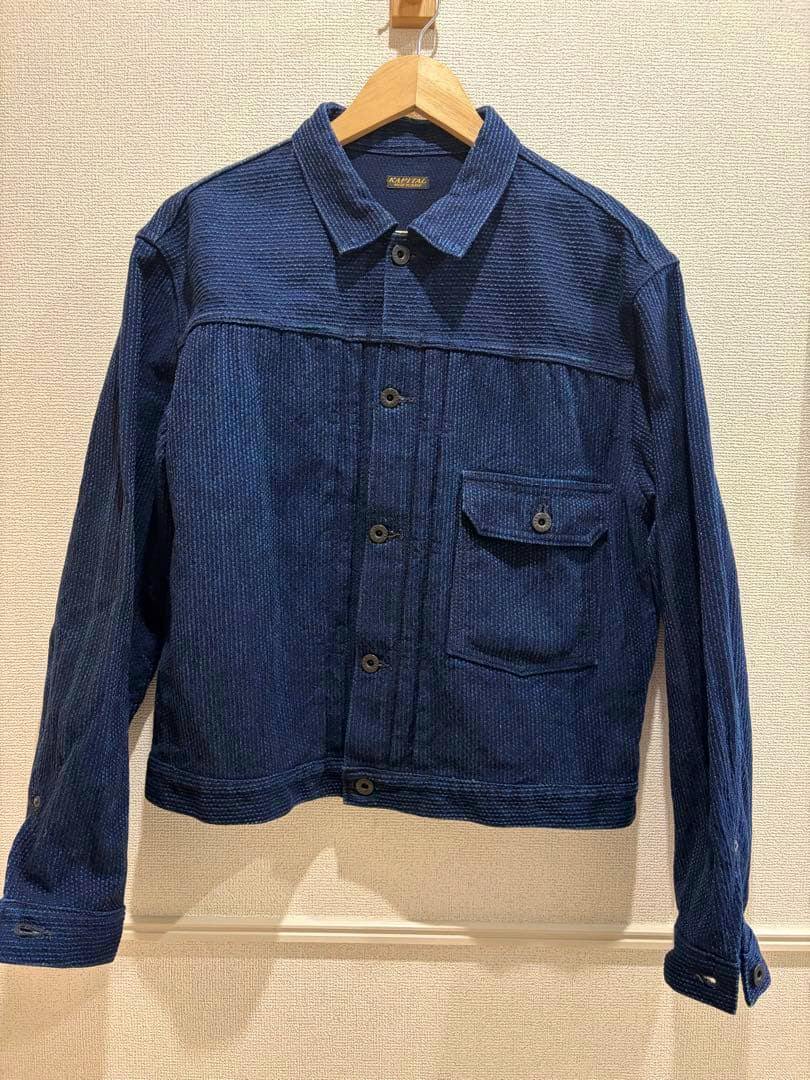 Front view of a blue Kapital Century Denim no.123 men's denim jacket hanging on a wooden hanger against a wall.