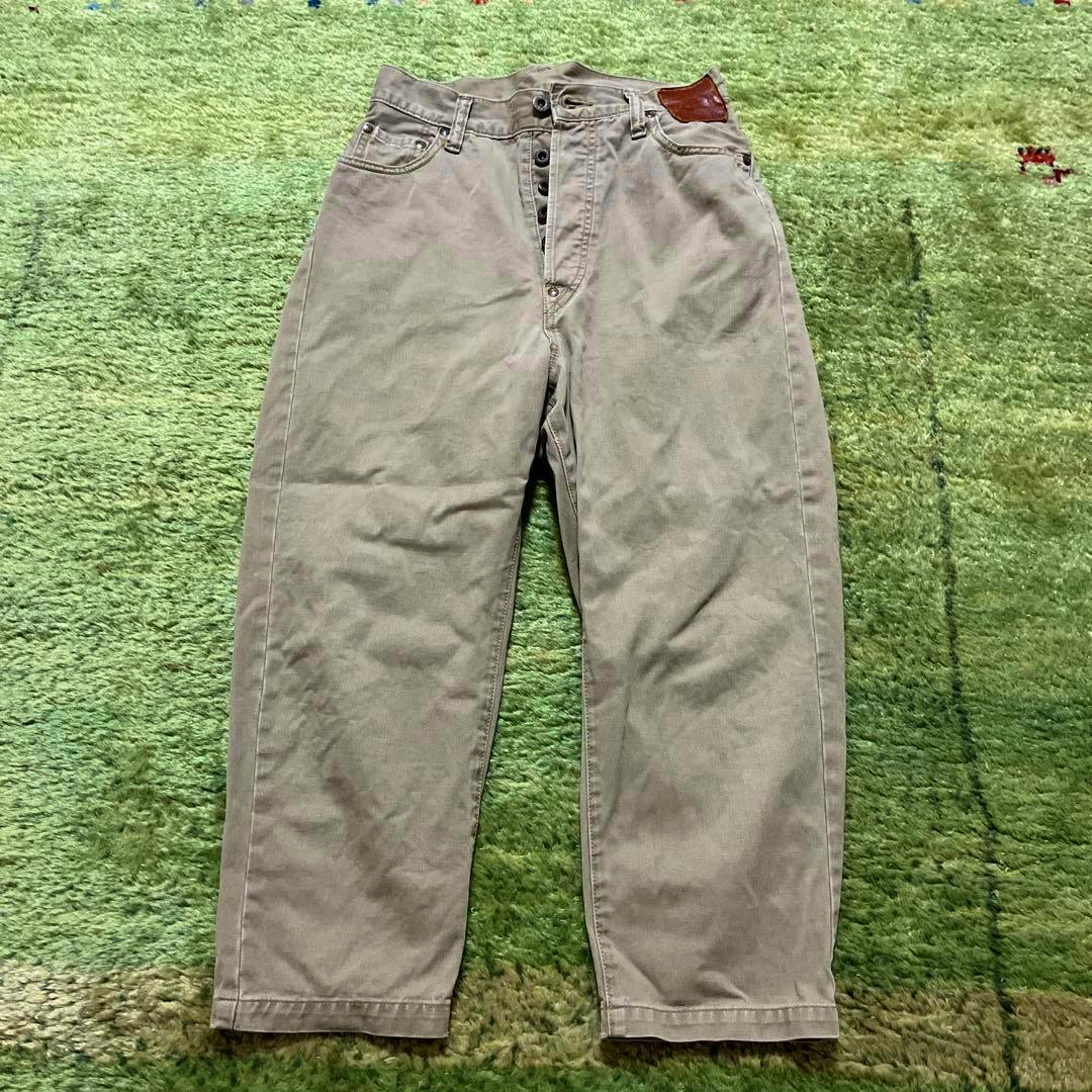 Front view of the men's tapered cotton pants laid flat on a green surface.