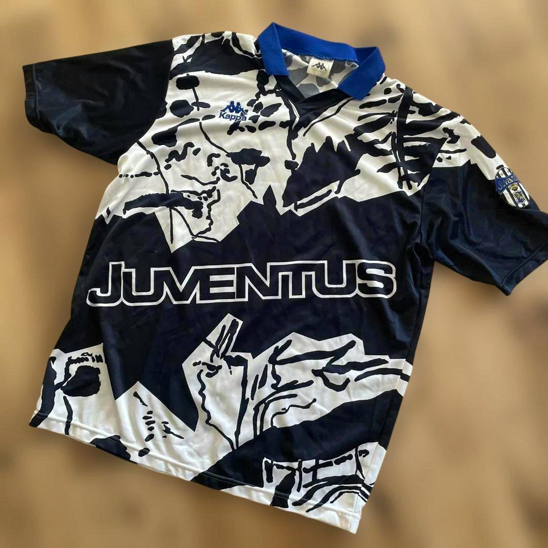 Front view of a Kappa Juventus football jersey laid flat, black-and-white patterned with 'JUVENTUS' across the front and a blue collar.
