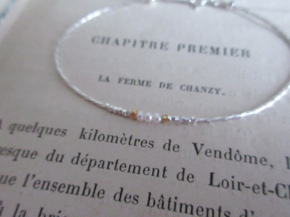 A thin silver-toned bracelet with a small cluster of baby pearls and tiny accent beads resting on a sheet of printed text.