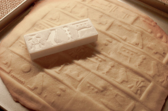 A rectangular cookie stamp mold with hieroglyph designs sits on a baked cookie showing matching stamped impressions.
