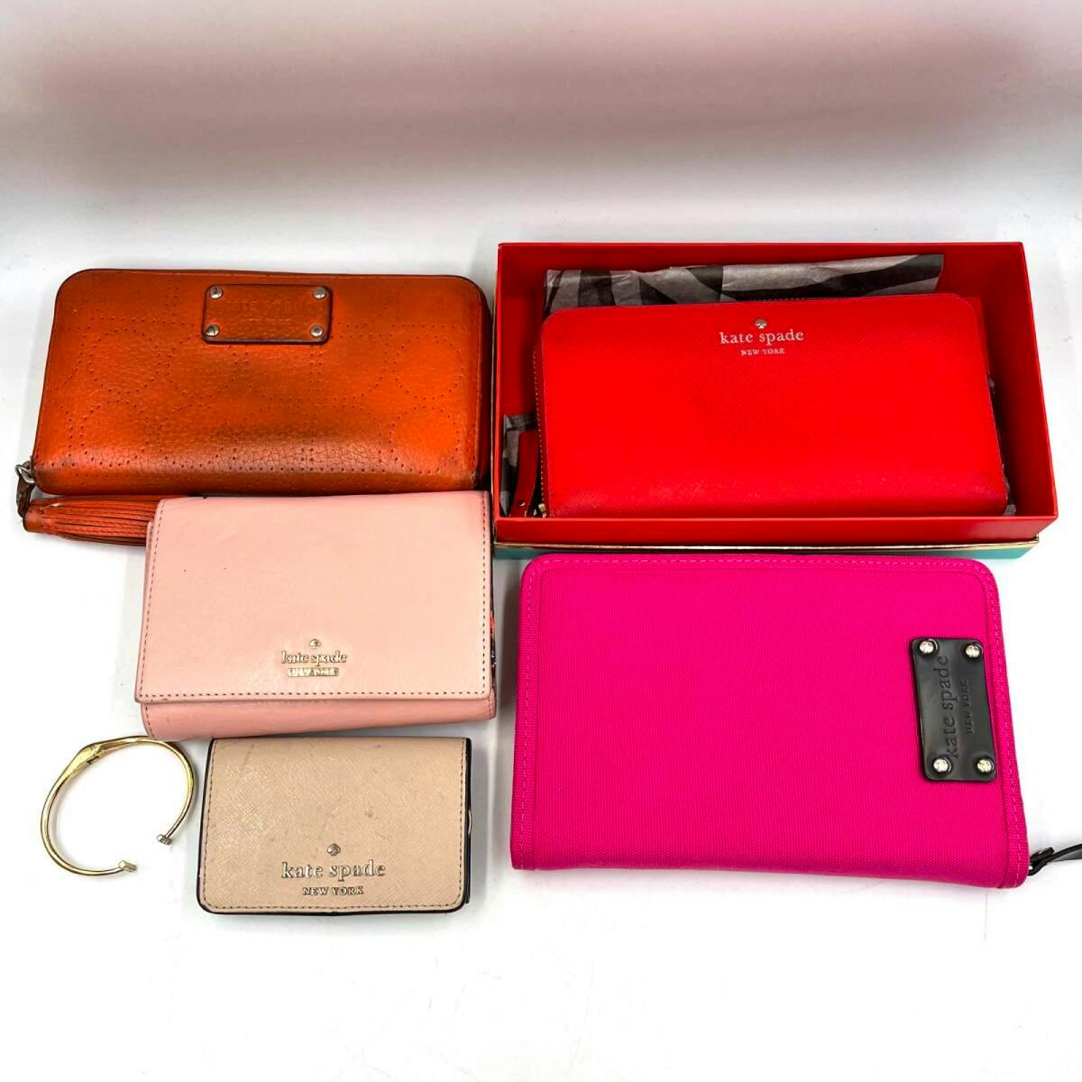 Six Kate Spade wallets, cases, and a gold bracelet arranged on a white background.