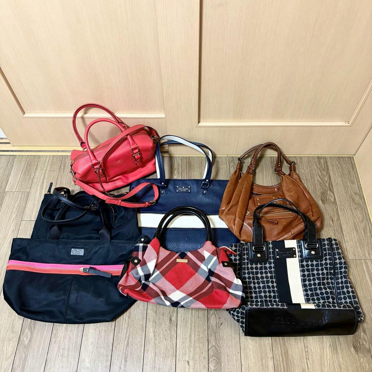 Seven assorted kate spade new york bags arranged on a wooden floor in front of a door.