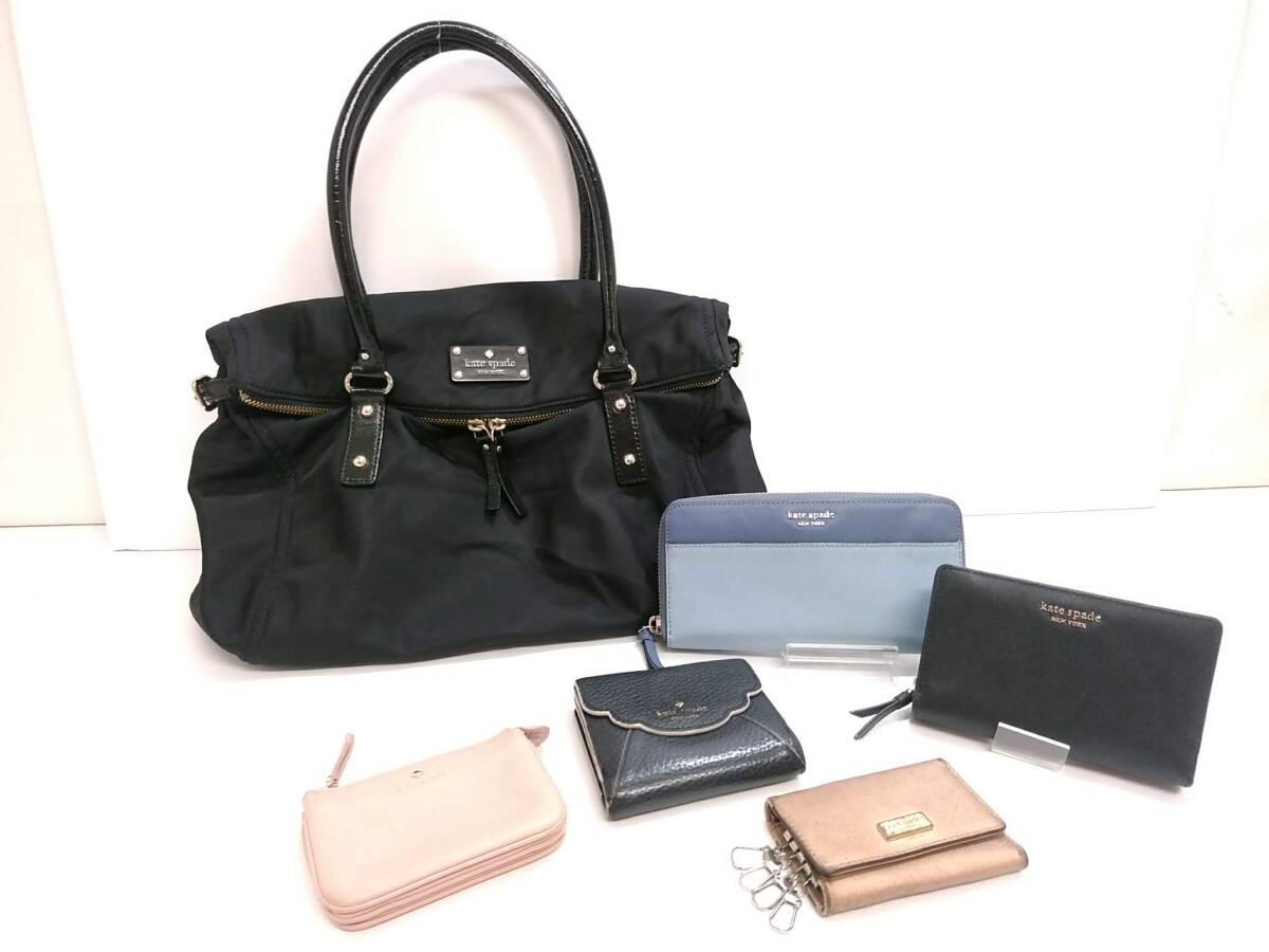 Black kate spade nylon handbag with several wallets and key cases arranged in front on a white background.