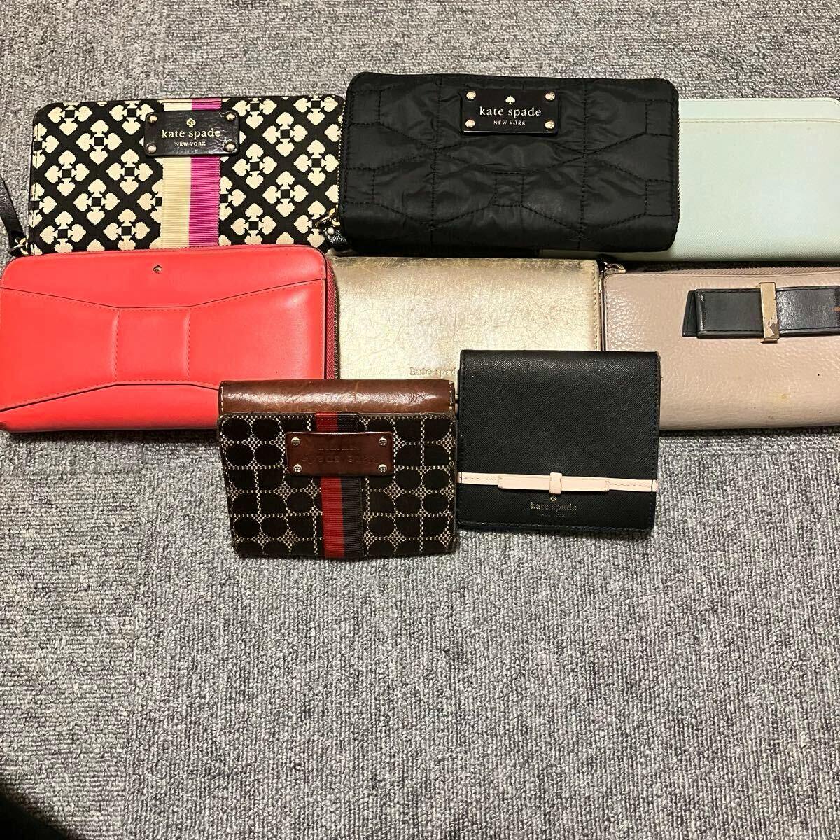 A set of eight Kate Spade wallets in various colors and styles arranged on a carpeted surface.