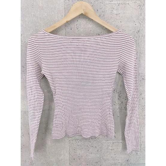 Pink and white striped long-sleeve T-shirt hanging on a wooden hanger against a concrete wall.