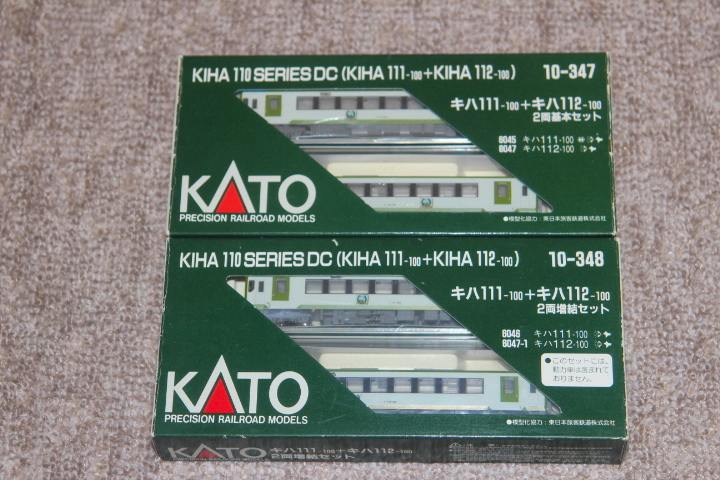 Two KATO KiHa 110 Series boxed model train sets (10-347 and 10-348) stacked on a carpeted surface.