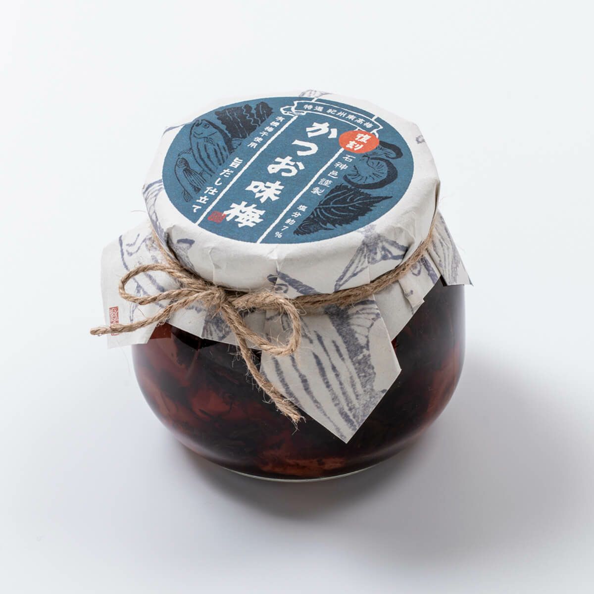 Glass jar of preserved plums with a paper-covered lid tied with twine, showing plums inside.
