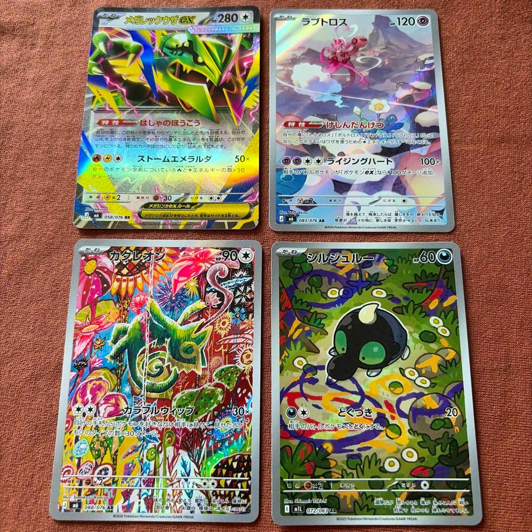 Four trading cards—カクレオン, ラブトロス, シルシュルー, and ARメガレックウザex RR—laid out on a reddish fabric background.