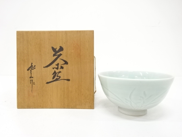 A porcelain tea cup displayed next to a wooden storage box with Japanese calligraphy.