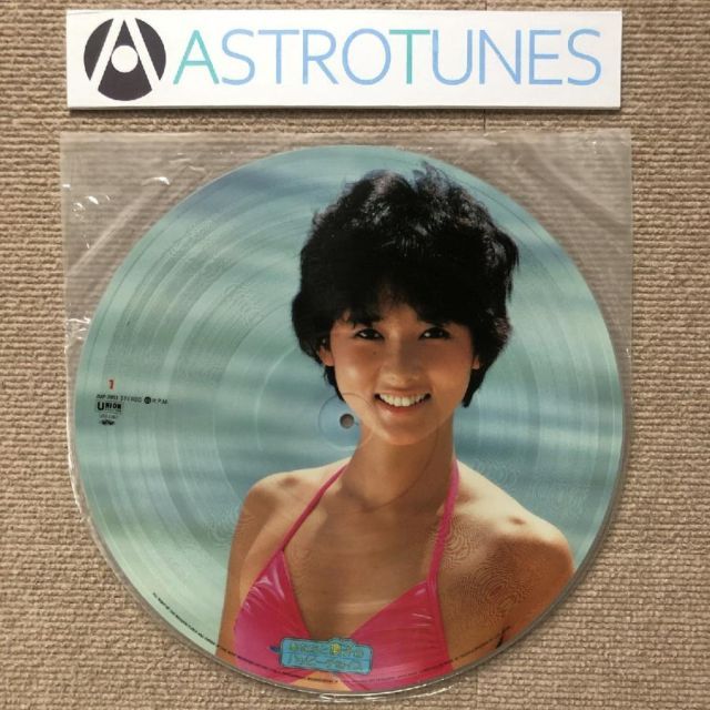 Picture-disc vinyl record showing a smiling woman in a pink swimsuit photographed on a carpeted surface with an ASTROTUNES label above.