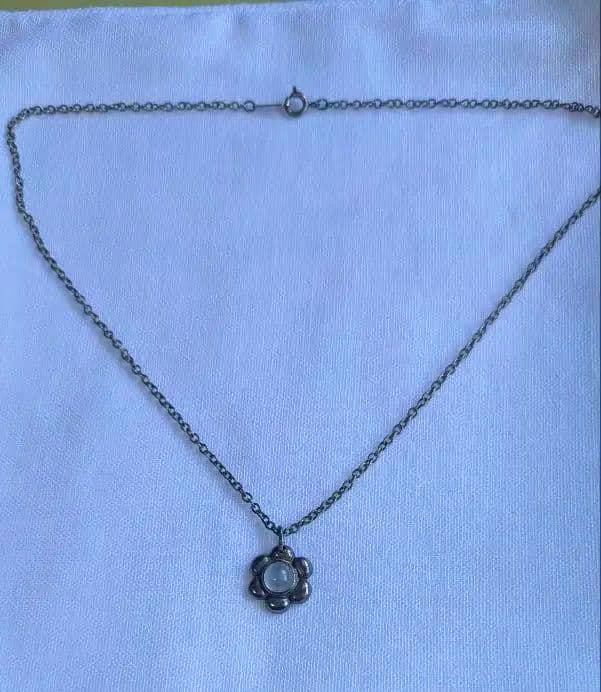 Metal chain necklace with a small flower-shaped pendant laid flat on a white cloth background.