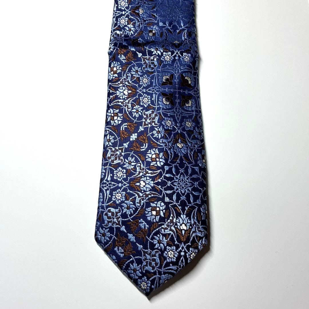 Blue silk necktie with a floral arabesque pattern displayed flat on a white background.