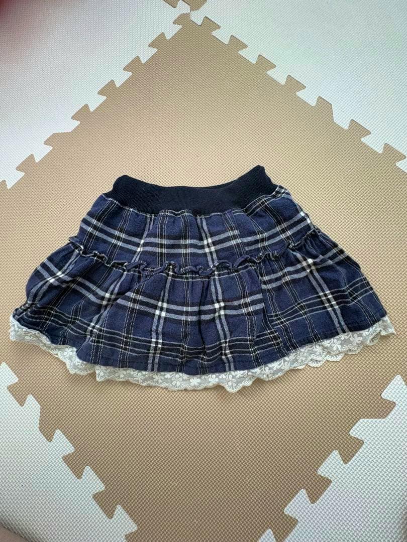 Navy check-pattern frill children's skirt (kids 110cm) laid flat on a foam play mat showing lace trim.