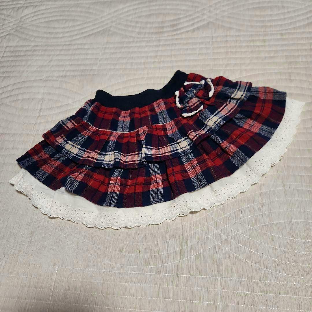 Kids' red and navy checkered tiered skirt with white lace trim laid flat on a surface.