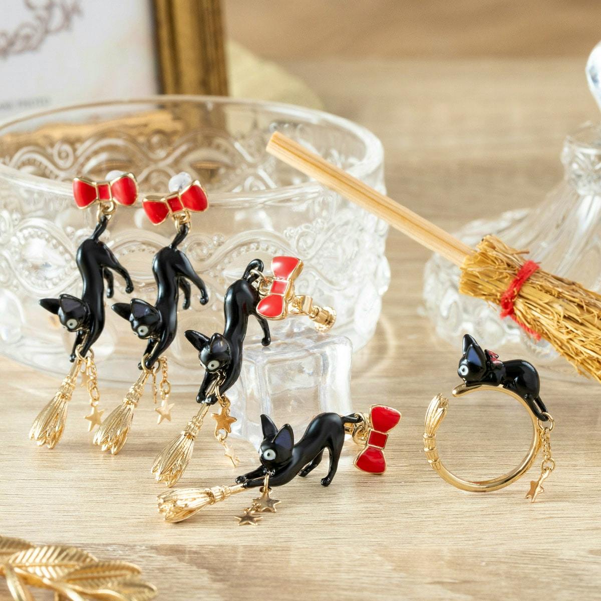 Photo of Jiji cat earrings with red bows and gold broom and star charms arranged on a wooden surface.