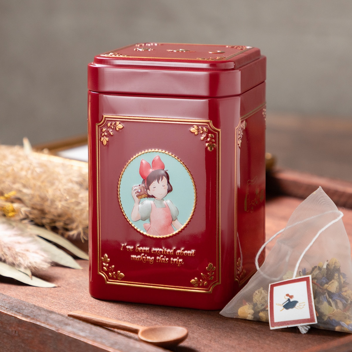 Red decorative tin for the 魔女の宅急便 (Kiki) original blend herbal tea with a pyramid tea bag beside it on a tabletop.