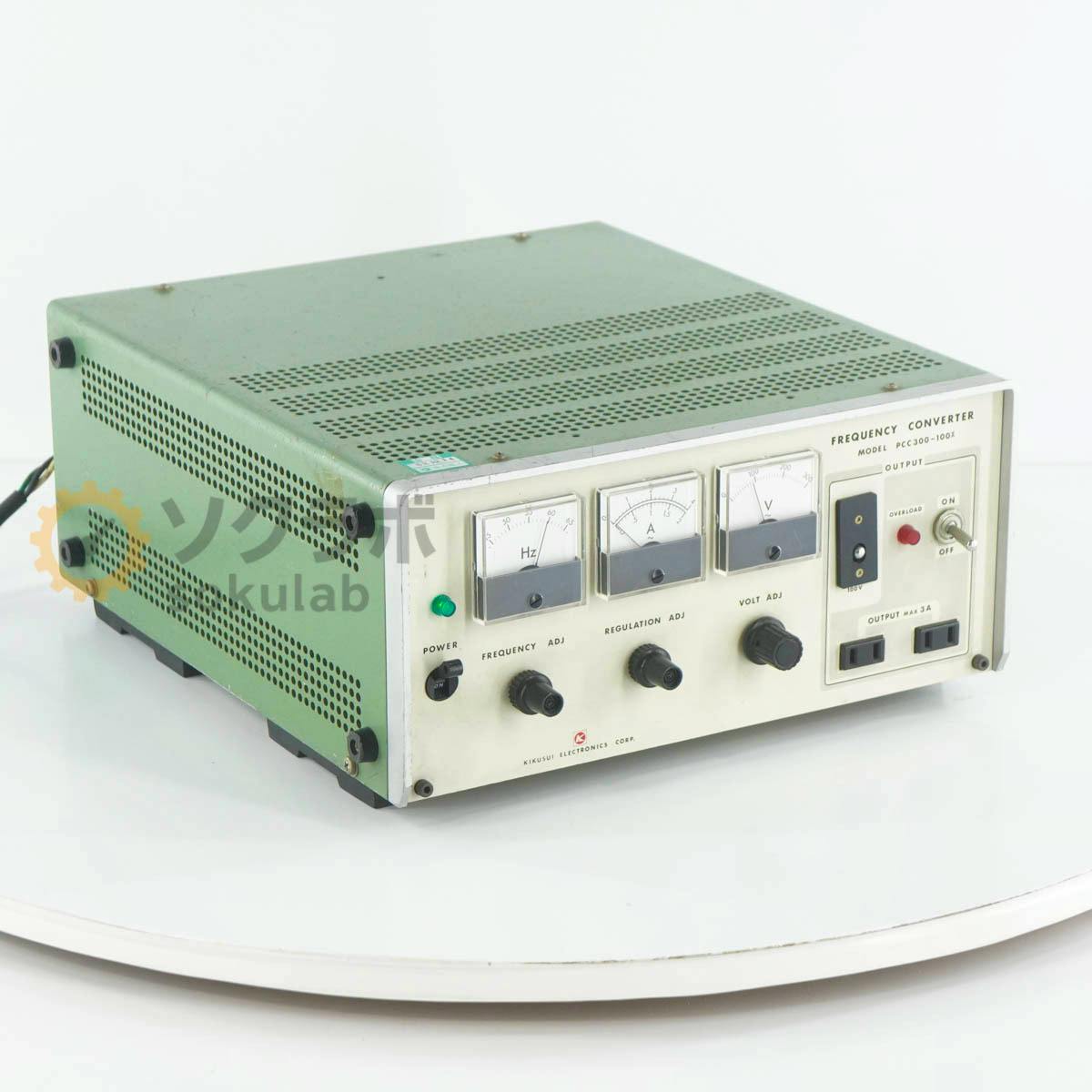 Front and side view of the KIKUSUI PCC300-100X frequency converter showing three panel meters, control knobs, and an output switch.